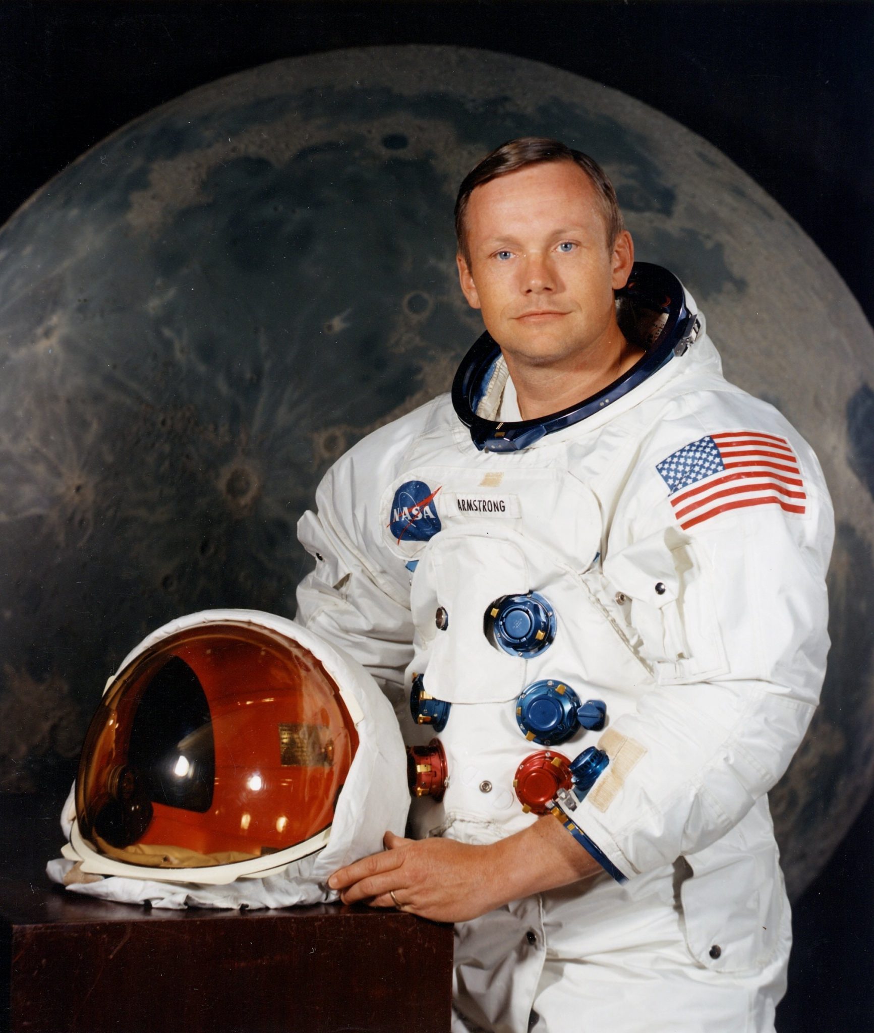 Neil Armstrong posing in front of moon backdrop while in astronaut gear holding helmet