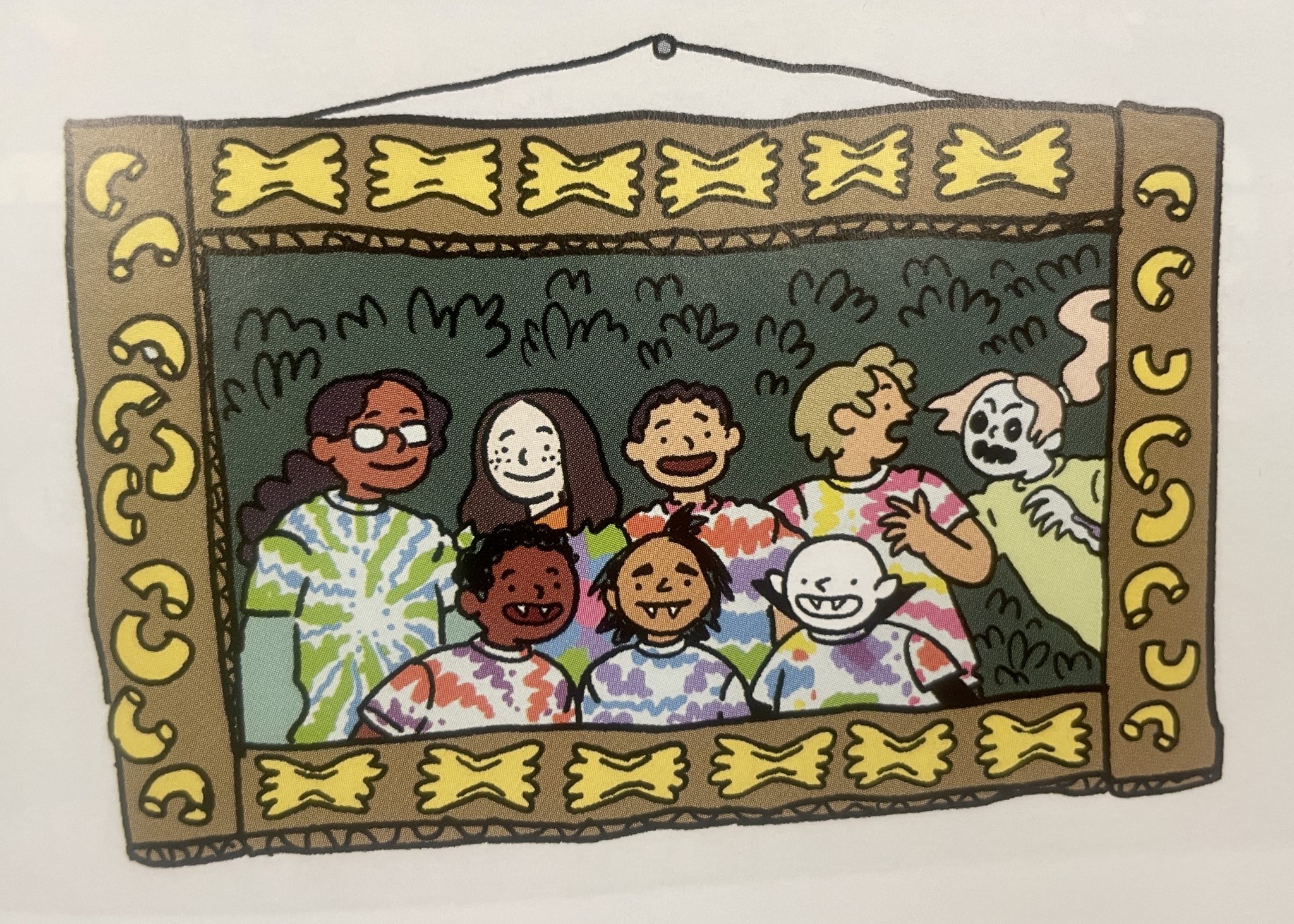 Page detail from "The Accursed Vampire: The Curse at Witch Camp," featuring a drawing of a cardboard picture frame with various dried pasta shapes glued onto the frame. Inside the frame is a photo of various children campers in tie-dyed tshirts. There are two rows of children in tie-dyed shirts standing in front of some bushes. The first row contains the main protagonists of the graphic novel, Quintus, Eztli, and Dragoslava, who are all vampire children. The second row contains four human campers. On the far right side of the photo, a zombie camper scares one of the alive children campers in the second row. 
