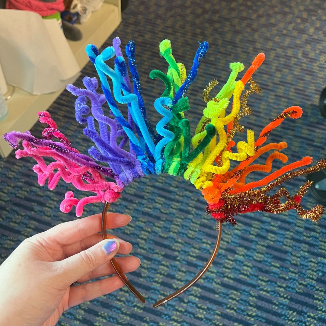 a person holding up a colorful headband made out of chenille stems