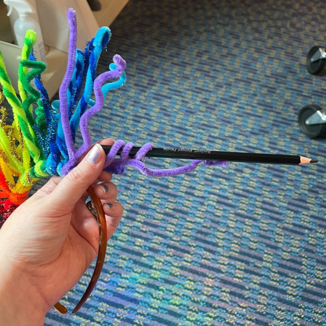 a person holding a rainbow chenille stem wrapped around a pencil in their hand