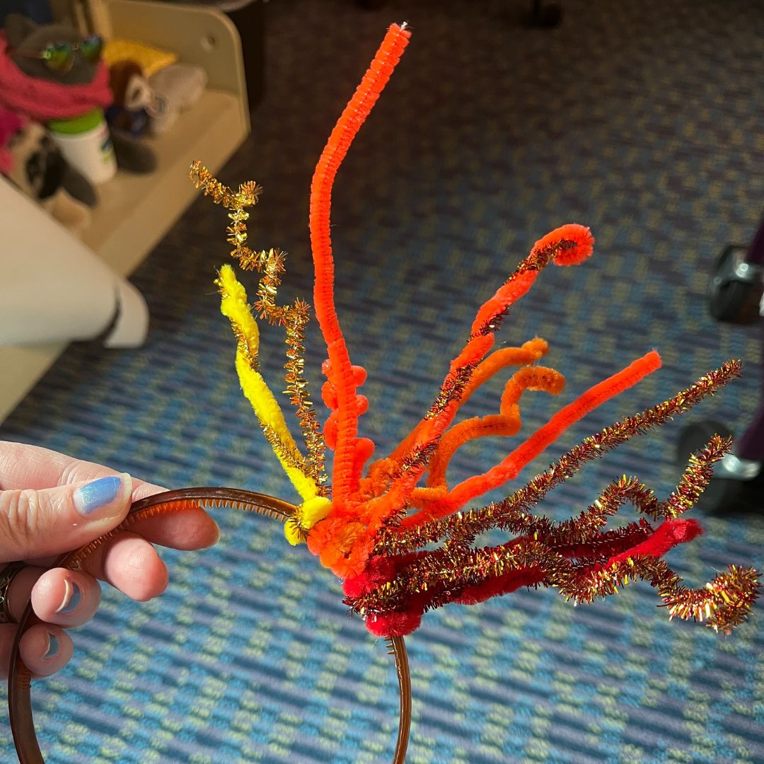 a person holding up a headband covered in red, yellow and orange chenille stems