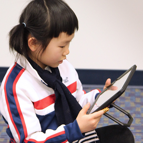 a child holds a digital tablet with both hands, looking down at it