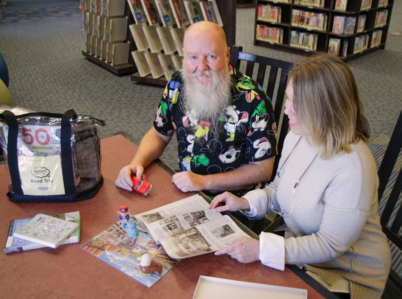 And older persona nd a younger one sit together at a table examining items from a library Memory Care Kit